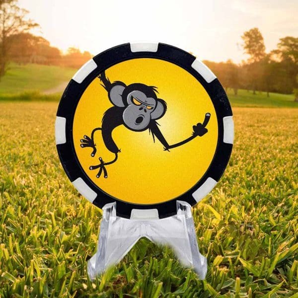 Black and white golf ball marker poker chip featuring a cheeky monkey swinging by and extending a one finger salute against a sunny yellow background.